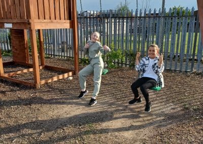 Two children leaping off the swings in the outdoor play area