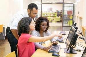 A tutor helping two learners at a computer