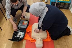 Two learners practising CPR and defibrillator use on a training manikin