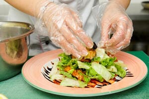 Gloved hands plating up a salad in a kitchen
