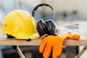 A hard hat, ear defenders, safety glasses and work gloves laid out on a bench