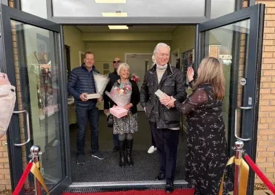 Guests stepping through the front doors of the centre onto a red carpet, carrying flowers and gifts.