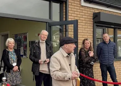 Guests and staff gathered outside the brick entrance of the centre behind a red rope.