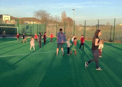 Younger children and their families playing games on the pitch in the winter sun