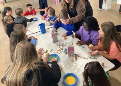 Children decorating buns around a big table with staff helping out
