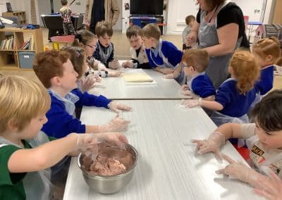Children with floury hands making dough along a long table