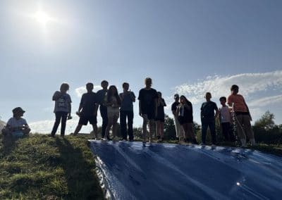 Young people lined up at the top of a giant blue slide in the sunshine