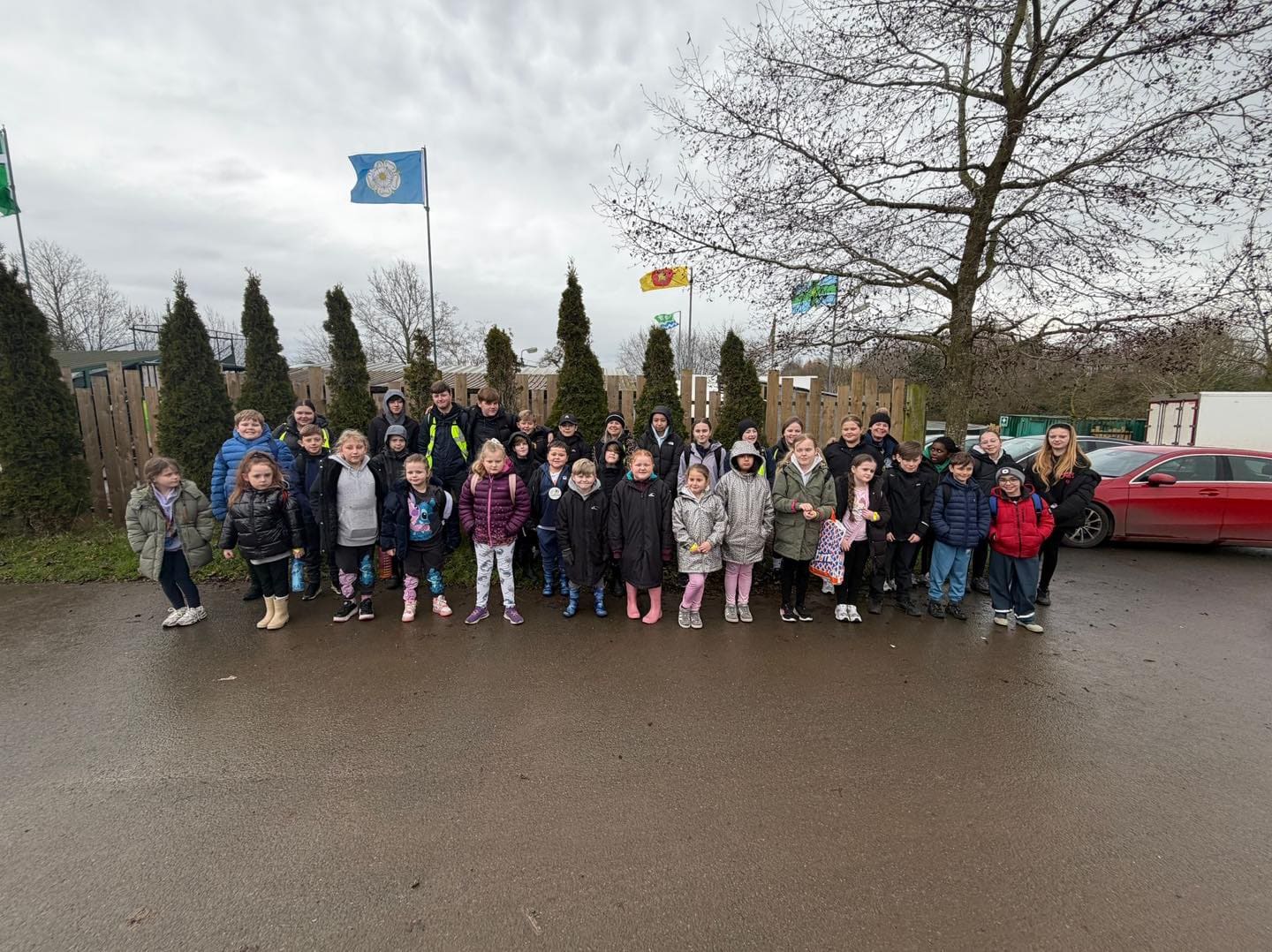 A large group of children wrapped up in winter coats, lined up outside on a wet day at the start of a trip.
