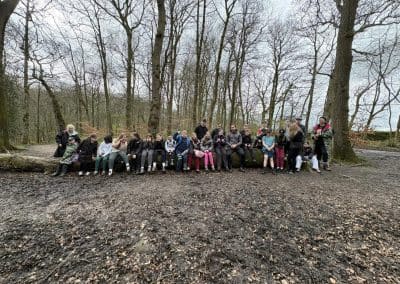 The group sitting along a fallen tree during a woodland walk