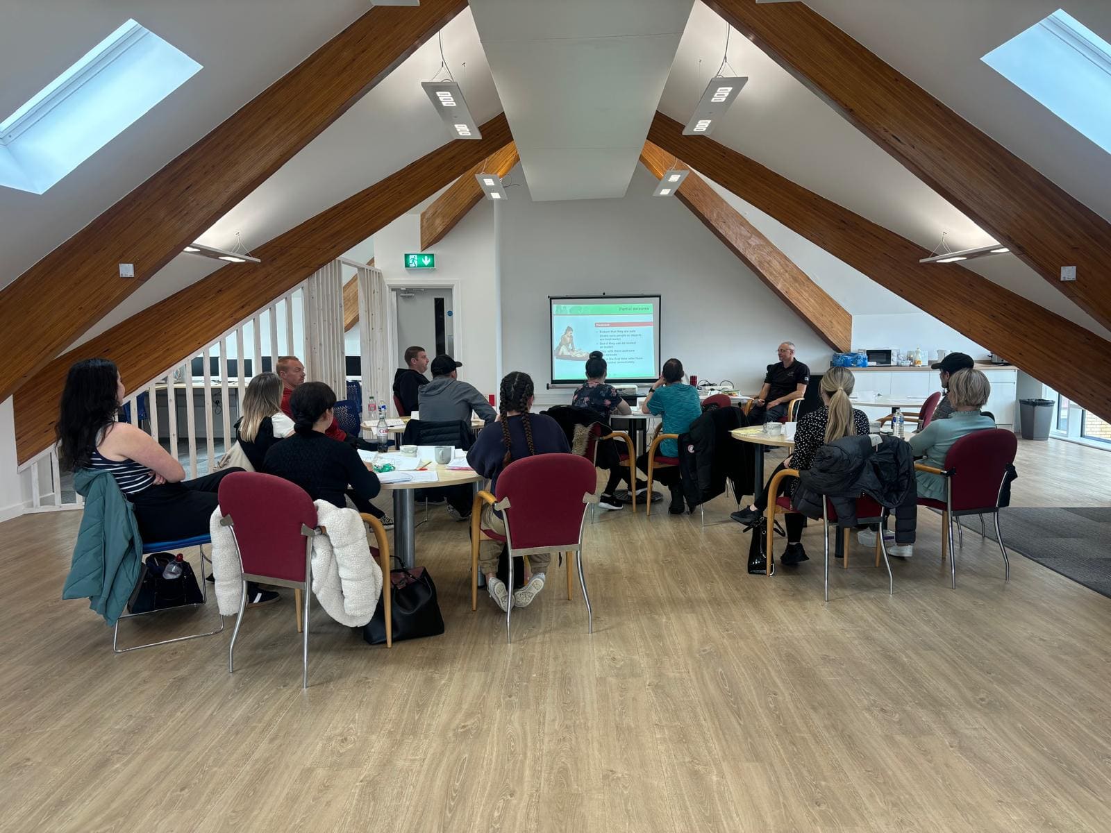 Adults sat around tables in the centre loft room taking part in a first aid training session.