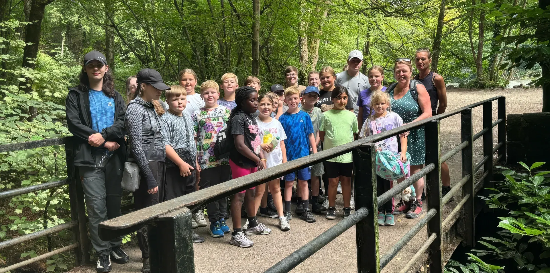 Children and youth workers stood together on a wooden footbridge in the woods during a summer trip.